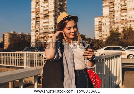 Smiling girl in the city with long board looking at phone.