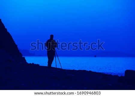 Silhouette of a male photographer by the sea during sunset it makes picturesque pictures of hills and landscapes on sunny summer evening. Nature photography concept. Advertising space
