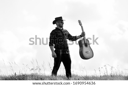 Country music concept. Guitarist country singer stand in field sky background. Country style. Summer vacation. Hiking song. Inspired country musician. United with nature. Handsome man with guitar.
