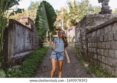 Beautiful and young slender girl poses as a model with a leaf on the island of Bali. The culture and nature of a tropical island is conveyed. Emotions and happiness