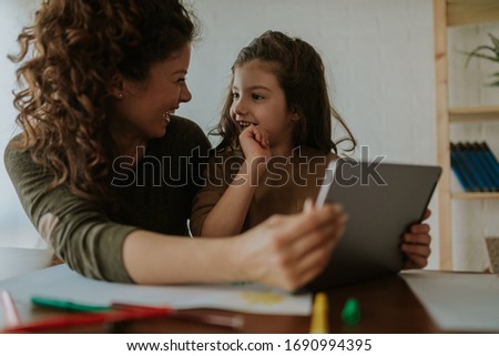Photo of happy mother and daughter fooling around at home. Mother and daughter are watching funny cartoons on tablet computer.