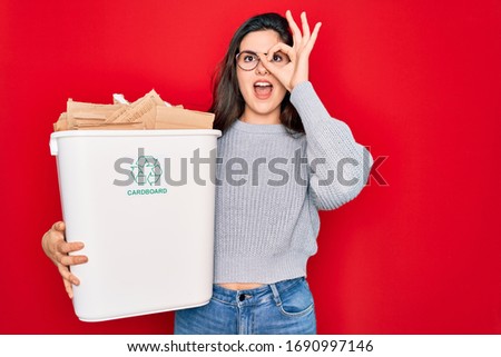 Young beautiful woman holding recycle cardboard containter recycling for eco environment with happy face smiling doing ok sign with hand on eye looking through fingers