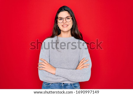 Young beautiful brunette woman wearing casual sweater over red background happy face smiling with crossed arms looking at the camera. Positive person.