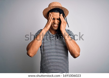 Young african american man with dreadlocks on vacation wearing striped t-shirt and hat suffering from headache desperate and stressed because pain and migraine. Hands on head.