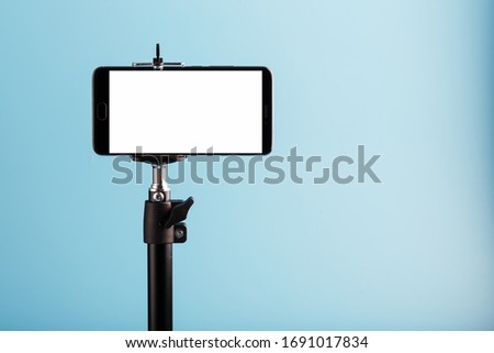 Mobile phone on a tripod with a clear white display for image and text, blue isolated background. Royalty-Free Stock Photo #1691017834