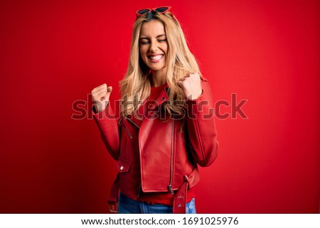 Young beautiful blonde woman wearing casual jacket standing over isolated red background excited for success with arms raised and eyes closed celebrating victory smiling. Winner concept.