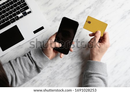 Mock-up of man hands-holding smartphone and using his credit card and laptop on marble surface.