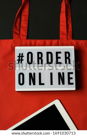 lightbox with words order online. Online shopping concept. Laptop with red cotton shopping bag on black background. Top view, flat lay, copy space. Zero waste, eco friendly , coronavirus concept