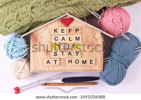 Knitting in qurantine concept.Home leisure composition.The inscription keep calm and stay home on little wooden house, knitting supplies: hooks, yarn, needles are lying around. Top flat lay.