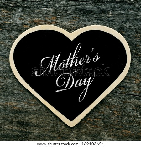 a heart-shaped blackboard with the text mothers day written in it on an old wooden surface