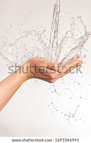 Photo of women's hands on which a stream of clean water pours. Human hands with falling water and spray isolated on white. Cleanliness and hygiene of the body. Girl's hand with water drops. 