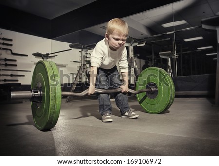 Determined young boy trying to lift a heavy weight bar Royalty-Free Stock Photo #169106972