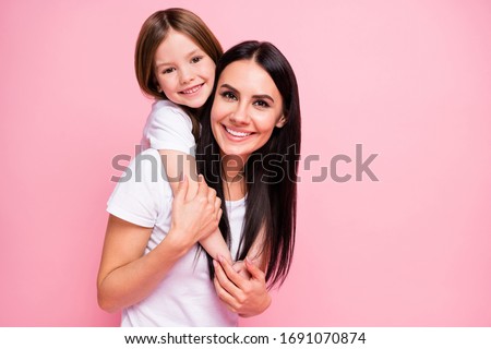 Photo of pretty young mommy hold arms hugging little daughter good mood lovely sincere cardiac feelings piggyback wear casual t-shirts jeans isolated pastel pink color background