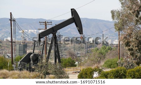 Industrial urban landscape. La Brea Inglewood in Los Angeles. Well pump jack operating behind the fence. Drilling rig extract crude oil. Oil mining machine with working piston. Oil and gas industry.