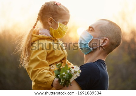 Family protection. A young father hugs his little girl daughter in the spring garden outdoors. Protective masks on faces from coronavirus infection Royalty-Free Stock Photo #1691089534