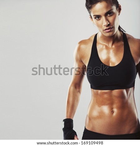 Picture of a fitness model on grey background. Young woman bodybuilder with muscular body looking at camera with copyspace