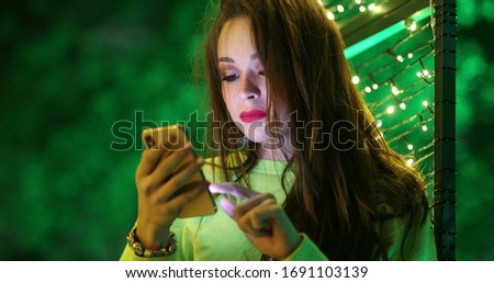 
Hispanic pretty brunette girl using her cellphone at night in city. Woman enjoying night-life while communicating with friends on her smartphone