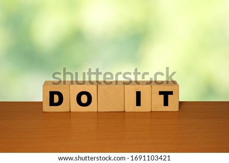 DO IT message word on a wooden desk on cube blocks with a green nature background
