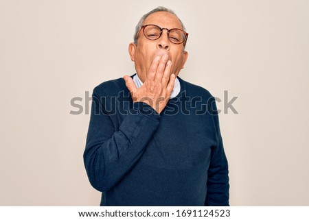 Senior handsome grey-haired man wearing sweater and glasses over isolated white background bored yawning tired covering mouth with hand. Restless and sleepiness.
