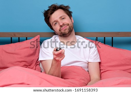 Caucasian man in bed using remote control for changing tv channel or air conditioning feeling bored or stressed. Studio shot