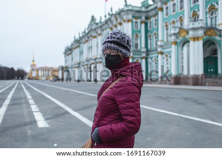 Side view of Young woman in black mask looking at camera. Empty dvortsovaya square in the centre of the city on background