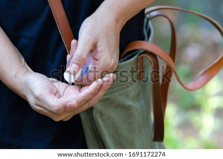 Woman's hands using portable wash hand sanitizer gel pump dispenser with alcohol gel sanitizer in bokeh green, Shoulder bag, Close up shot, Select focus, Prevention from covid19, Bacteria, Healthcare