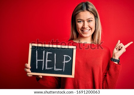 Young beautiful woman holding blackboard standing over isolated red background very happy pointing with hand and finger to the side