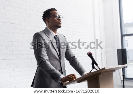confident african american business speaker standing on podium with microphone in conference hall Royalty-Free Stock Photo #1691202010