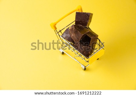 Pieces of dark chocolate in a grocery cart isolate on yellow background close-up, copy space