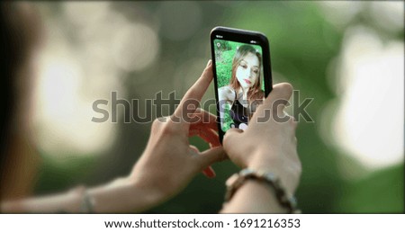 
Pretty girl in her 20s taking selfie with smartphone device outside at park. Young woman takes photo of herself with phone