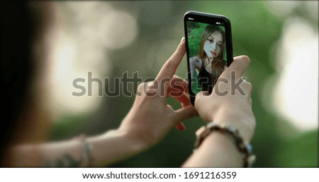 
Pretty girl in her 20s taking selfie with smartphone device outside at park. Young woman takes photo of herself with phone