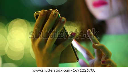 
Pretty girl looking at smartphone screen at night outside. Young millennial woman communicating touching cellphone device