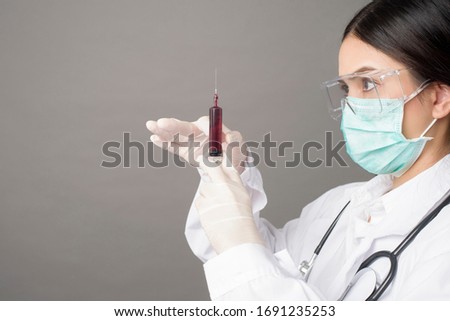 Doctor woman with surgical mask is holding hypodermic syringe 