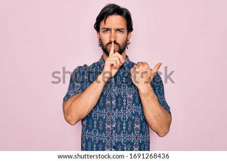 Young handsome hispanic bohemian man wearing hippie style over pink background asking to be quiet with finger on lips pointing with hand to the side. Silence and secret concept.