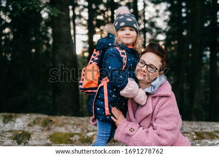 picture of lovely young caucasian female with pretty face, short dark hair, big eyes sits on the felled trees and plays with her child
