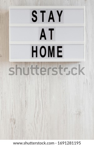 'Stay at home' words on a lightbox on a white wooden background, top view. Overhead, from above, flat lay. Copy space.