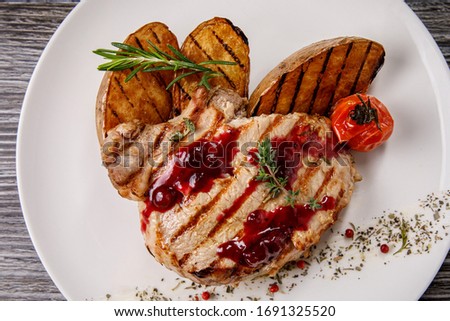 A piece of pork with a texture from a grill rack. The garnish of potatoes and tomato. White plate