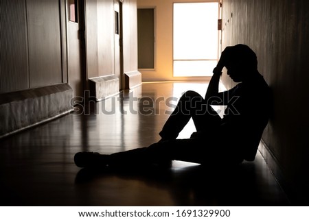 Silhouette of depressed man sitting on walkway of residence building. Sad man, Cry, drama, lonely and unhappy concept.