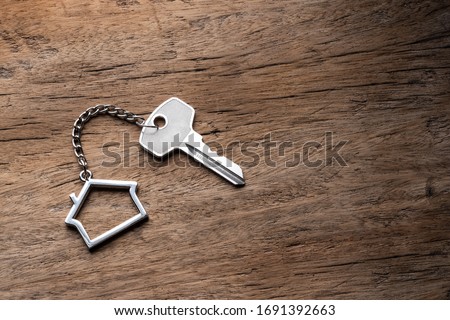 House key with home keyring decorated with mini heart on rusty wood background, copy space