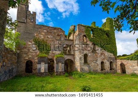 Inner garden of Clifden Castle ruins, walls covered with climbing plants, sunny spring day with blue sky and white clouds in County Galway, Ireland