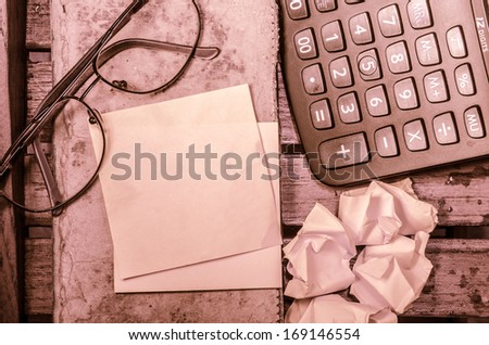 yellow blank paper with calculator with crumpled paper with glasses with pencil on an old book on 