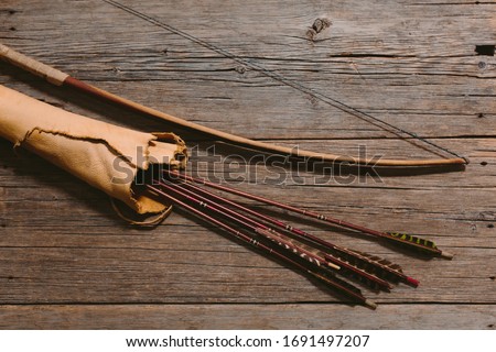 Close up shot of bow laying beside arrows in a leather quiver on wooden planks Royalty-Free Stock Photo #1691497207