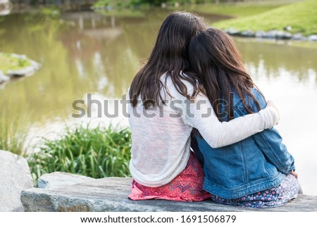 Two loving sisters hugging overlooking pond