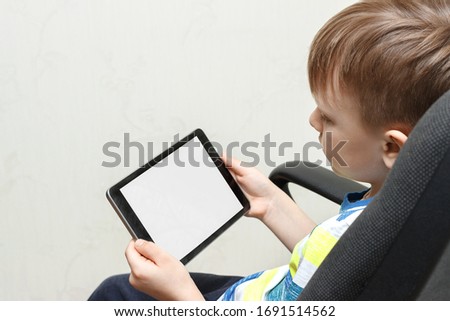 Modern generation. The child plays games or watches cartoons. The boy holds in his hands a tablet with a white screen for the layout.