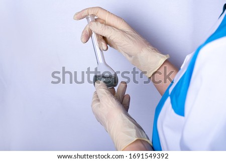 a nurse in uniform is holding a flask with a gray catalyst inside. hands in rubber gloves. personal protective equipment scientific experiments. chemical stuff
 Royalty-Free Stock Photo #1691549392
