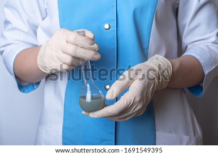 a nurse in uniform is holding a flask with a gray catalyst inside. hands in rubber gloves. personal protective equipment scientific experiments. chemical stuff
 Royalty-Free Stock Photo #1691549395
