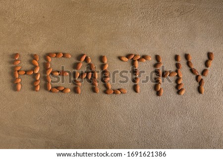 Nuts.The word healthy made from almonds on a beige concrete background