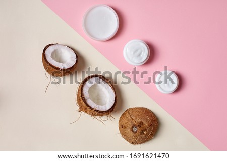 Concept of healthy and natural beauty products. Top view of half coconut lying near container with moisturizer cream on background with pastel color