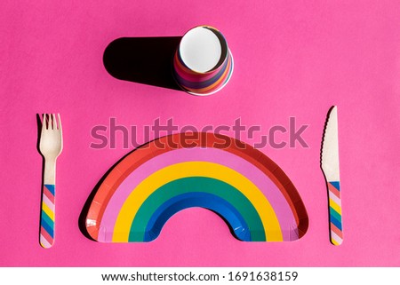 cutlery set, rainbow plate and paper and wood cup with LGTBI motifs on pink background. conceptual image