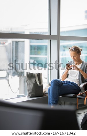 Casual blond young woman using her cell phone while waiting to board a plane at departure gates at international airport.